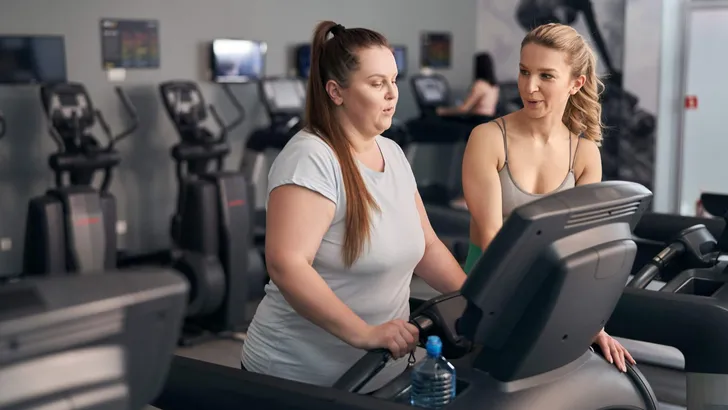 Caucasian instructor helping plus size woman at the gym