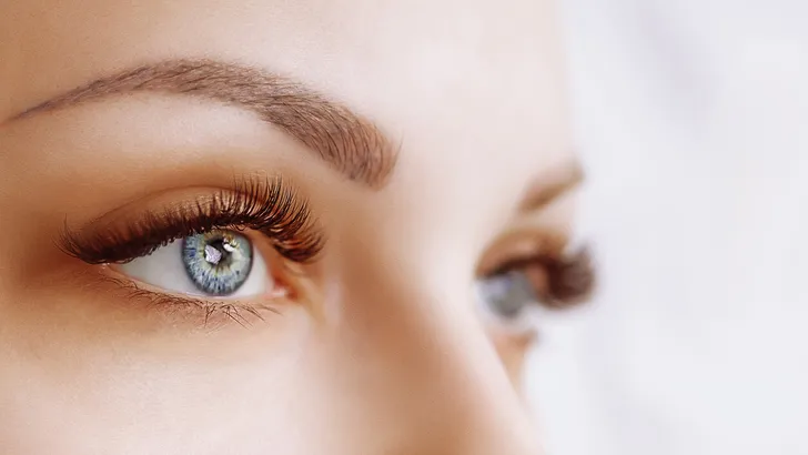 Eyelash Extension Procedure. Woman Eye with Long Eyelashes. Close up, selective focus