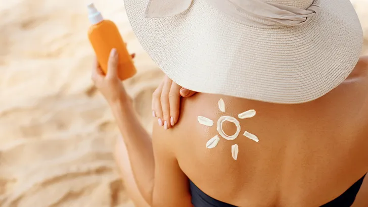 Vrouw die op het strand zit en zonnebrand vasthoudt