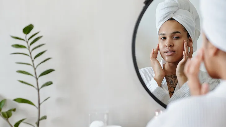 Young woman with towel on head touching her face after beauty procedure