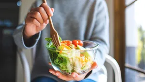 Close-upfoto van een vrouw die een kom met verse gemengde groentesalade eet en vasthoudt met een vork.