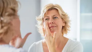 Mid adult woman spreading a layer of facial cream in front of the mirror