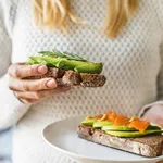 Close up of woman holding plate with avocado toast as fresh snack, day light.