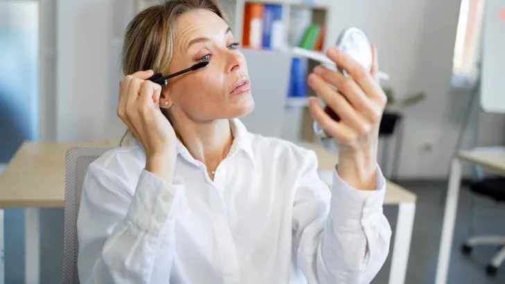 Middle aged business woman in formal wear applying mascara