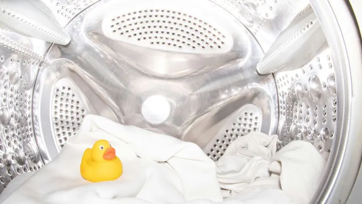 Een gele badeend samen met beddengoed in een wasmachine trommel