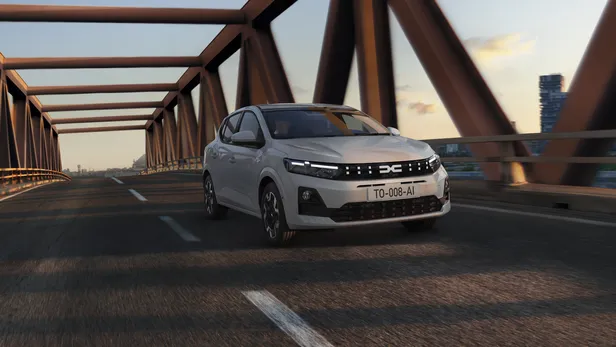 Witte Dacia Sandero rijdt over een stalen brug bij zonsondergang.