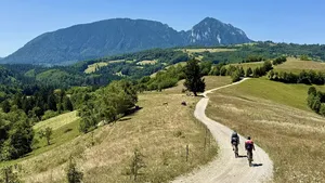 Een gravelbiker fietst over een witte onverharde weg door het groene heuvellandschap van Transsylvanië, met in de achtergrond een traditioneel dorpje en kerk.