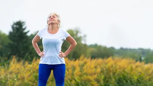 Volwassen vrouw neemt even pauze van het sporten in de buitenlucht met haar handen in de zij, kijkt omhoog.