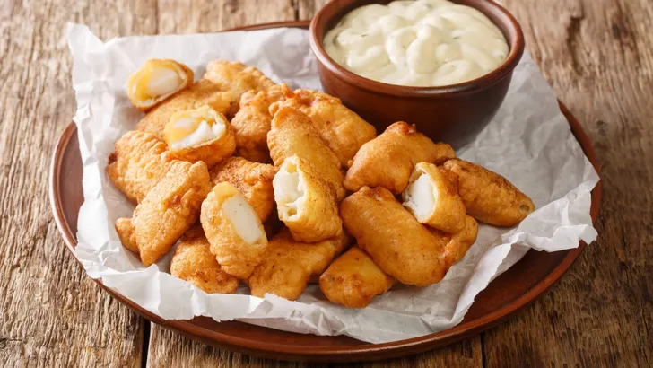Fish appetizer consisting of deep-fried cod pieces and served with a dipping sauce closeup in the plate on the table. Horizontal