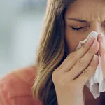 Shot of an attractive young woman feeling ill and blowing her nose with a tissue at home