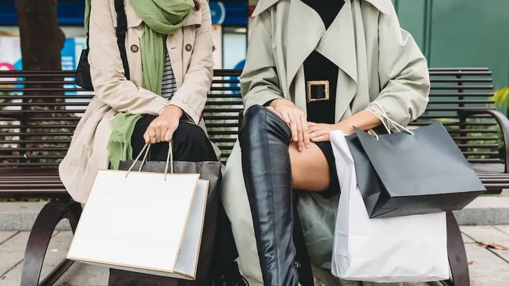 Crop women sitting on bench with shopping bags