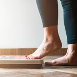 Female checking kilogrammes getting on the scale - self care and body positivity concept - warm flare on left