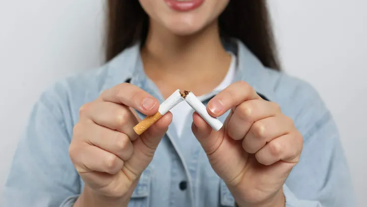 Stop smoking concept. Woman breaking cigarette on light grey background, closeup