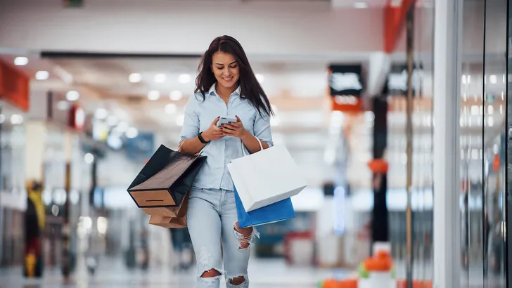 Brunette woman in the supermarket with many of packages and phone in hands have shopping day