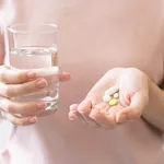 Sick, asian young woman, girl hand holding pill capsule, painkiller medicine from stomach pain, head ache, pain for treatment, take drug or vitamin and glass of water at home, pharmacy and health care