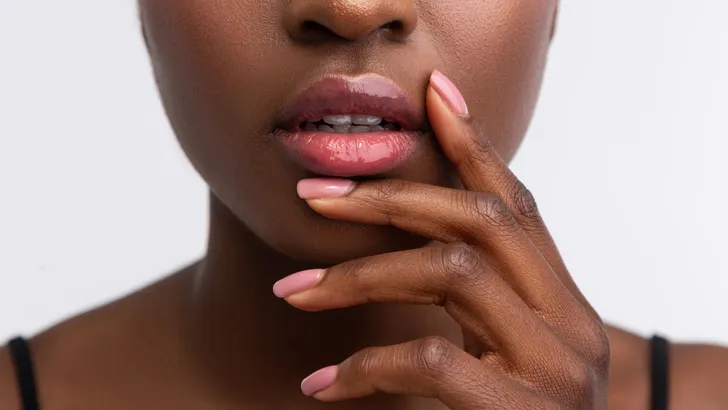African-American woman touching lips with shiny lip gloss