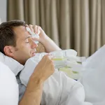 Man sick in bed drinking hot drink