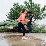 Two beautiful women running in park with rain and puddles.