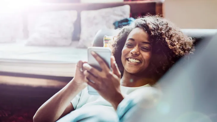 Happy woman using mobile phone on sofa