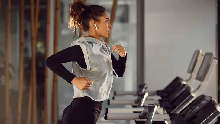 Side view of female athlete running on treadmill in a gym.