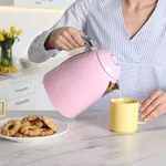 Woman pouring hot water from modern electric kettle in cup indoo