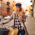 Young woman using a smartphone while pushing her bicycle in the city