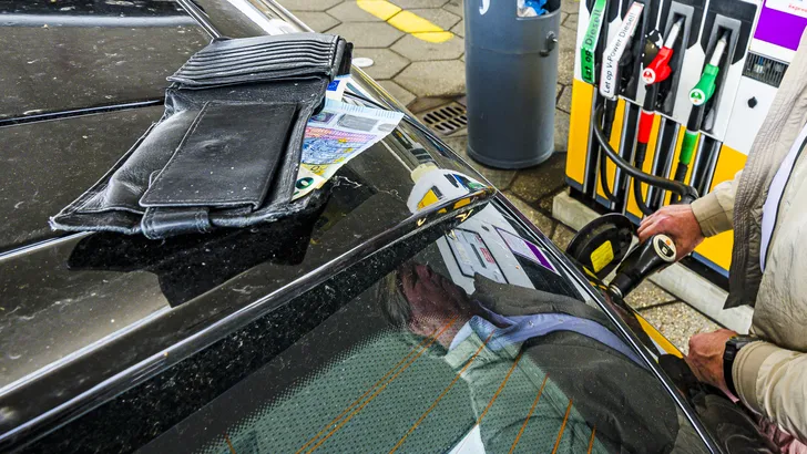 Iemand tankt een auto, terwijl op het dak een portemonnee met een briefgeld ligt.
