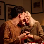 Happy young couple hugging laughing drinking wine on Valentines day at home.