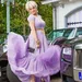 Marjan Strijbosch, bekend van The Real Housewives van het Zuiden, in een lila jurk bij verschillende luxe auto's.