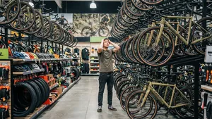 Een man staat met zijn handen in het haar van keuzestress in een overvolle fietsenwinkel, omringd door rekken vol gravelbikes en accessoires.