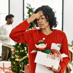 Young hispanic woman standing by christmas tree with decoration tired rubbing nose and eyes feeling fatigue and headache. stress and frustration concept.