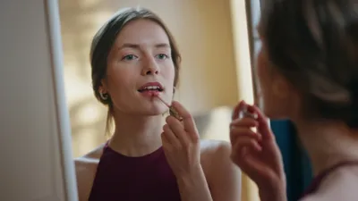 Vrouw brengt glanzende lippenstift aan in een spiegel, close-up.