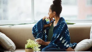 Thoughtful young female wrapped in blanket having coffee on sofa at home
