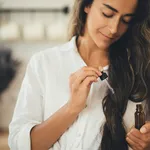 Young woman applying natural organic essential oil on hair and s