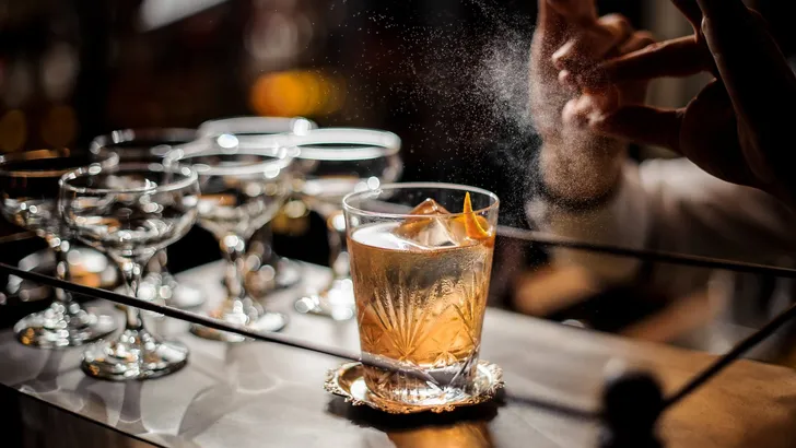 Bartender decorating fresh old fashioned summer cocktail with ice and orange peel