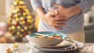 Buikpijn na maaltijd tijdens de feestdagen, met kerstboom op de achtergrond.