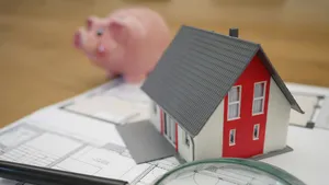 Beleggen in vastgoed. – Foto van miniatuur-huisje op plattegrond bij spaarvarken.