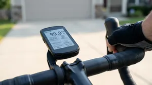 Een close-up foto van een fietscomputer op een racefiets stuur dat 99,9 km aangeeft, met een fietser die naar huis fietst op de oprit.