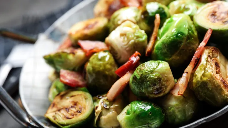 Delicious Brussels sprouts with bacon in dish on table, closeup