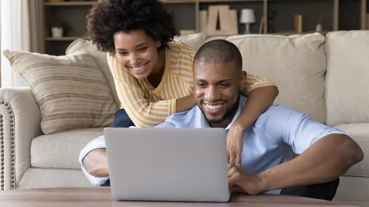 African couple sit in living room have fun use laptop