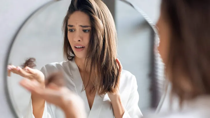 Hairloss Concept. Worried Young Woman Holding Bunch Of Fallen Hair In Hand