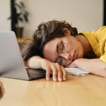 Young tired woman in eyeglasses sleeping on desk with laptop at