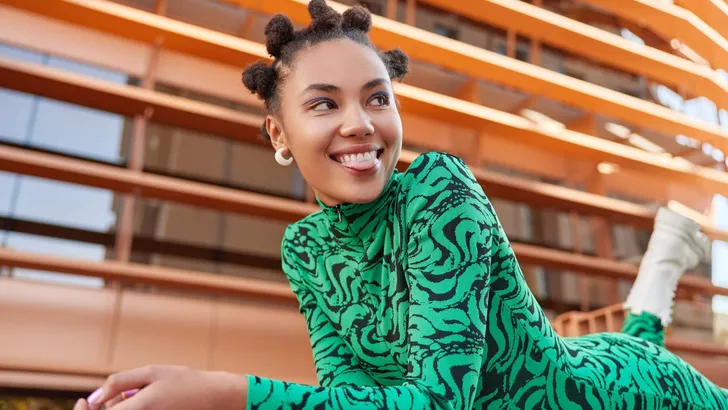 Relaxed pretty millennial girl lies on stomach wears green comfortable bodysuit sticks out tongue looks away with happy expression has vivid makeup playful mood. People emotions style concept