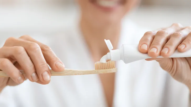 Uitsnede van een vrouw die tandpasta op een tandenborstel knijpt.