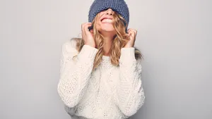Portrait of beautiful blond woman in white in white sweater and blue hat