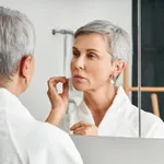 Beautiful senior woman wearing bathrobe standing in front of a mirror