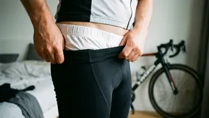 Close-up van een fietser die een fietsbroek aantrekt waarbij de rand van de onderbroek zichtbaar is boven de tailleband, als voorbeeld van een veelgemaakte beginnersfout.
