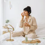 Smiling woman applying face cream sitting on bed