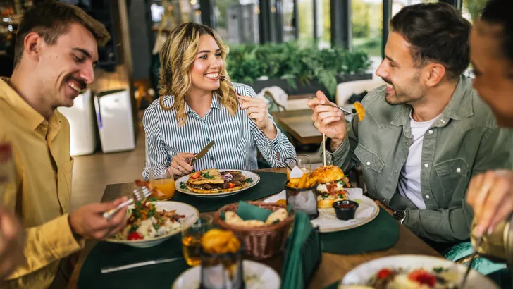 Groep vrienden is samen aan het eten in een restaurant. Ze eten salades, hamburgers, brood en vlees.