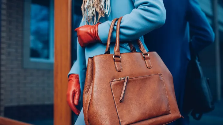 Weekendtips van Beau Monde – Close-up foto van leren tas aan arm van vrouw in wollen blauwe wintermantel.